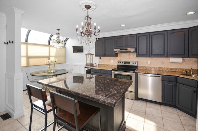 kitchen with appliances with stainless steel finishes, a kitchen island, decorative light fixtures, dark stone counters, and light tile patterned flooring