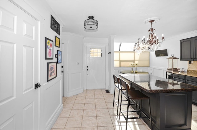 kitchen with light tile patterned flooring, ornamental molding, a center island, a kitchen bar, and dark stone countertops