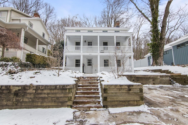 snow covered house featuring a balcony and a porch