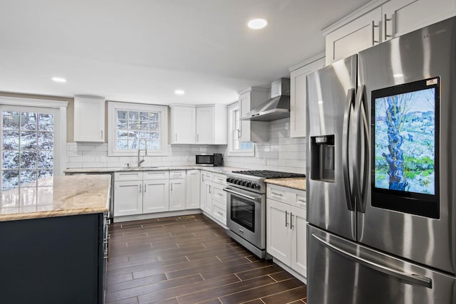 kitchen featuring appliances with stainless steel finishes, wall chimney exhaust hood, sink, white cabinets, and light stone counters