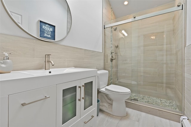 bathroom with tile walls, a baseboard heating unit, vanity, a shower with shower door, and toilet