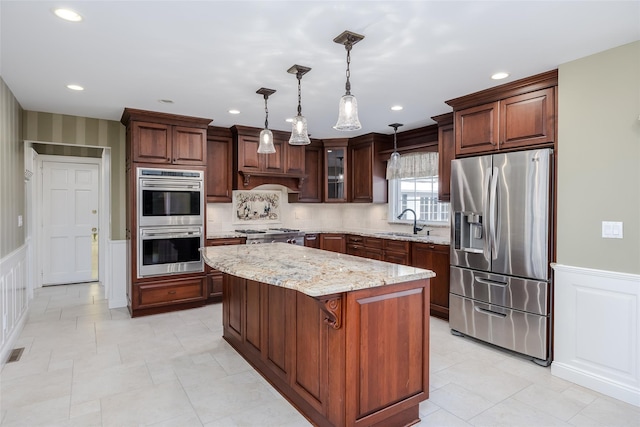 kitchen featuring sink, a center island, hanging light fixtures, stainless steel appliances, and light stone countertops