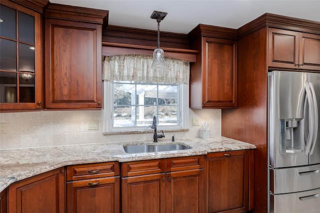 kitchen featuring decorative light fixtures, tasteful backsplash, sink, stainless steel fridge, and light stone countertops