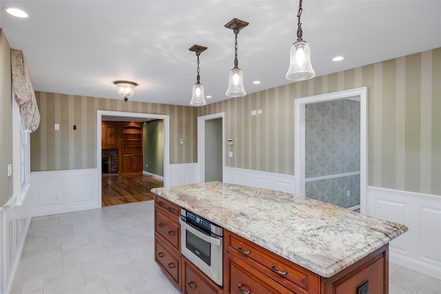 kitchen with light tile patterned floors, a center island, light stone countertops, a brick fireplace, and decorative light fixtures