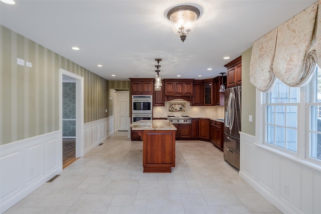 kitchen featuring stainless steel appliances, a kitchen island, pendant lighting, and light stone counters