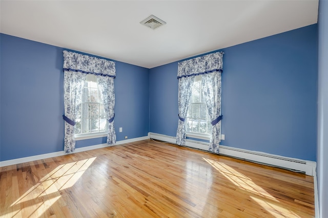 spare room featuring wood-type flooring, baseboard heating, and plenty of natural light