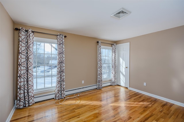 spare room with plenty of natural light, a baseboard heating unit, and hardwood / wood-style floors