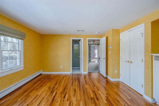 unfurnished bedroom featuring light hardwood / wood-style flooring, a baseboard radiator, and ensuite bathroom