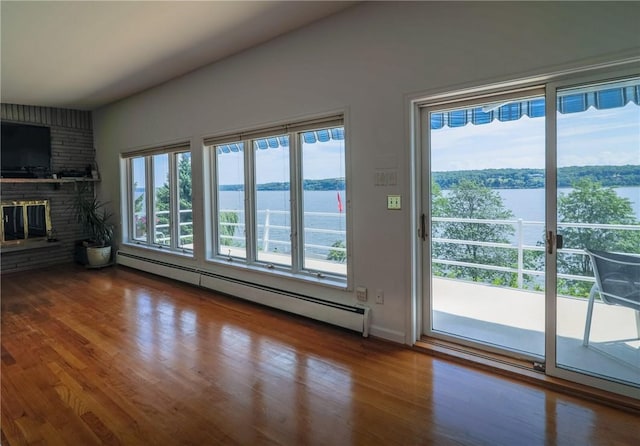 unfurnished living room with a brick fireplace, a water view, wood-type flooring, and a baseboard radiator