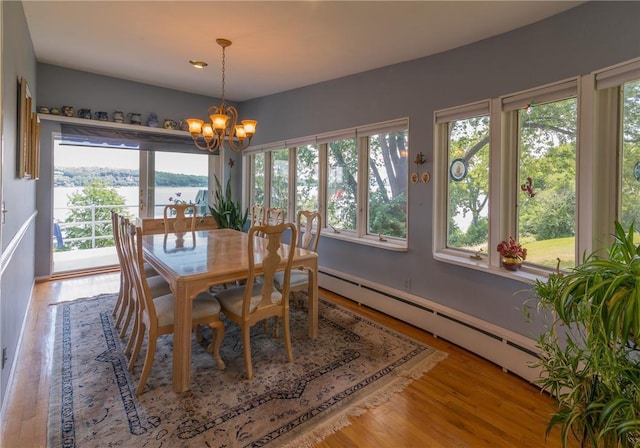 dining room featuring a water view, baseboard heating, a notable chandelier, and wood-type flooring