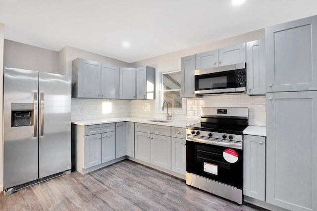 kitchen featuring stainless steel appliances, gray cabinetry, decorative backsplash, light wood-type flooring, and sink