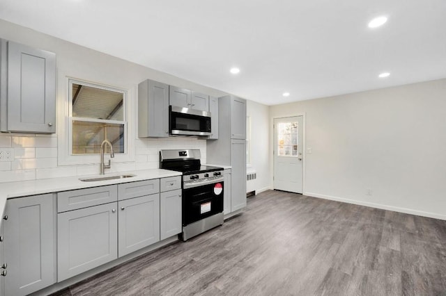 kitchen with appliances with stainless steel finishes, radiator heating unit, sink, gray cabinets, and light hardwood / wood-style flooring