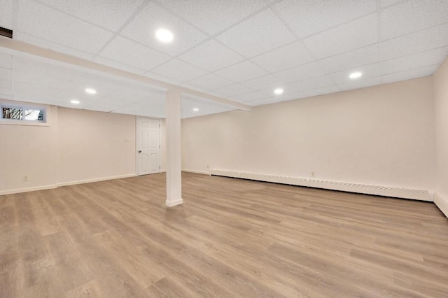 basement featuring baseboard heating, a drop ceiling, and light hardwood / wood-style flooring