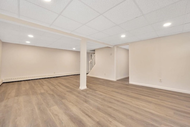 basement with light wood-type flooring, a drop ceiling, and a baseboard radiator