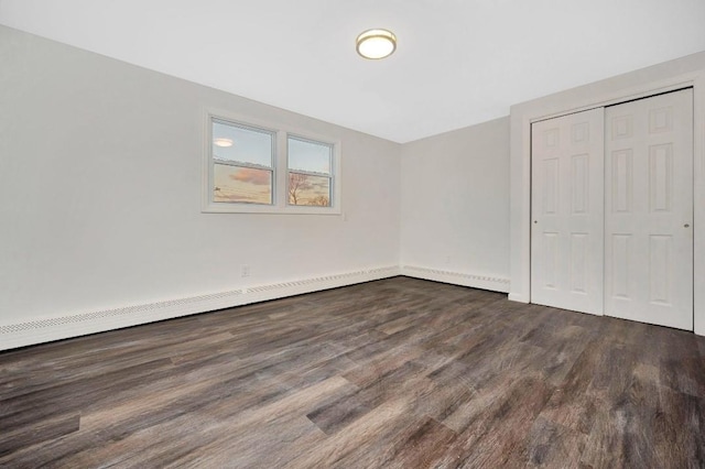 unfurnished bedroom with a baseboard heating unit, dark wood-type flooring, and a closet