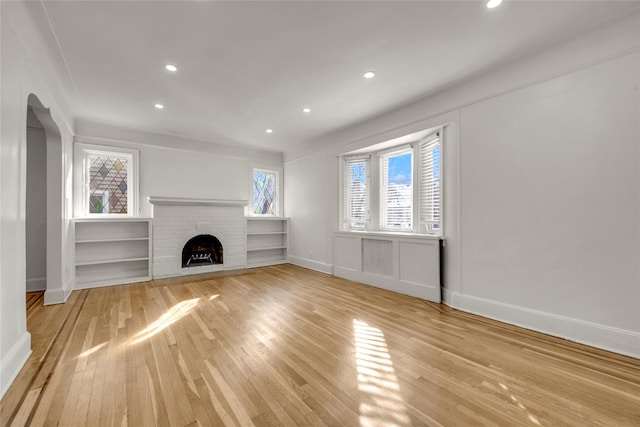 unfurnished living room featuring a brick fireplace, light hardwood / wood-style flooring, and built in features