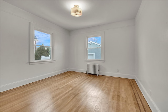 unfurnished room with radiator, light hardwood / wood-style floors, and a healthy amount of sunlight