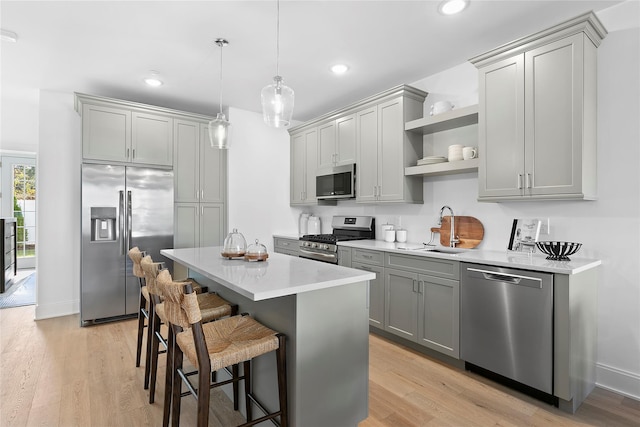 kitchen featuring a center island, stainless steel appliances, hanging light fixtures, gray cabinets, and light hardwood / wood-style flooring