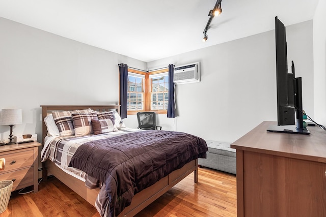 bedroom featuring rail lighting, a wall mounted air conditioner, and light wood-type flooring