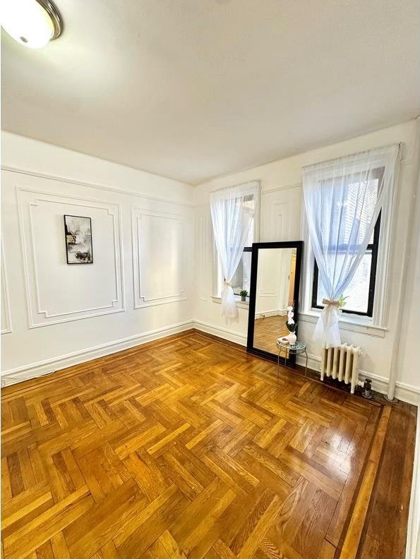 empty room featuring a healthy amount of sunlight, radiator heating unit, and a decorative wall