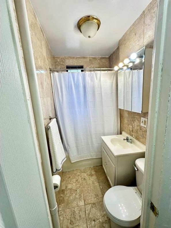 full bath with tile walls, shower / tub combo with curtain, toilet, and vanity