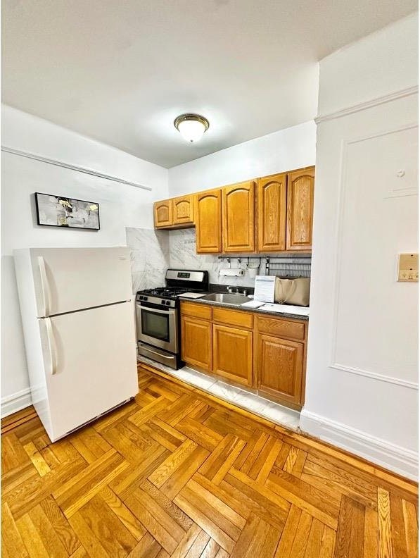 kitchen with brown cabinetry, freestanding refrigerator, a sink, decorative backsplash, and stainless steel gas range oven