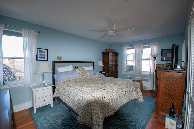 bedroom featuring a ceiling fan, wood finished floors, radiator heating unit, cooling unit, and baseboards