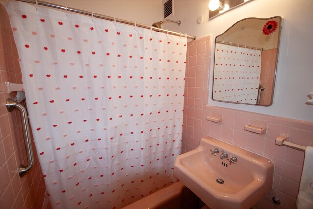 bathroom featuring tile walls, shower / bath combination with curtain, visible vents, and a sink