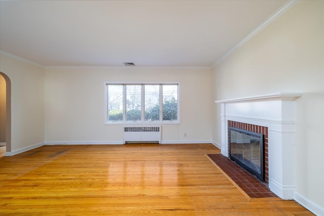 unfurnished living room featuring crown molding, radiator heating unit, light hardwood / wood-style floors, and a brick fireplace