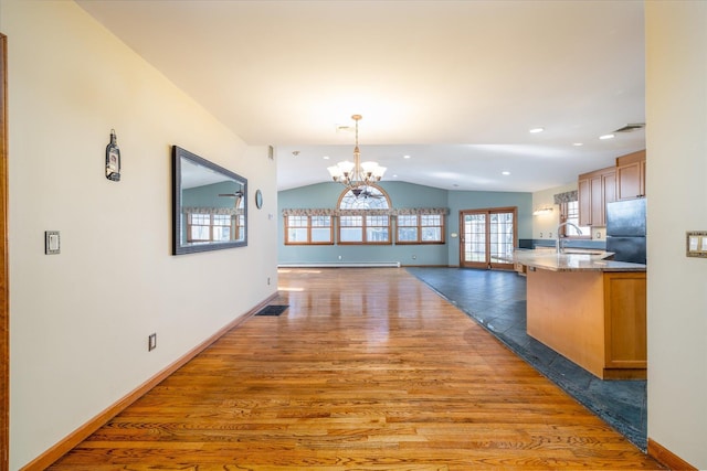 unfurnished dining area with vaulted ceiling, a baseboard heating unit, sink, dark wood-type flooring, and an inviting chandelier