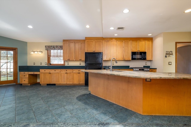 kitchen with light stone counters, sink, stove, and a healthy amount of sunlight