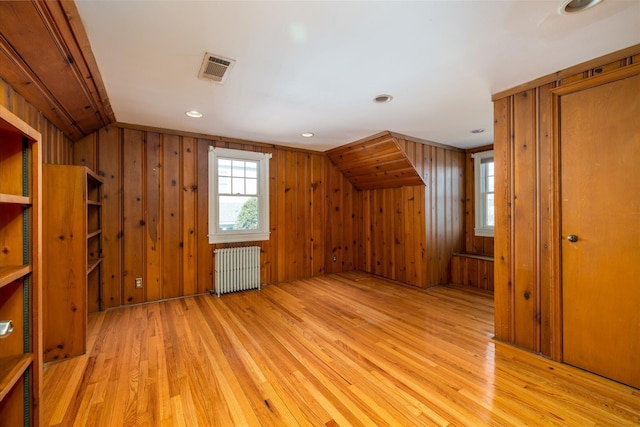 bonus room featuring light hardwood / wood-style flooring, radiator heating unit, wood walls, and vaulted ceiling