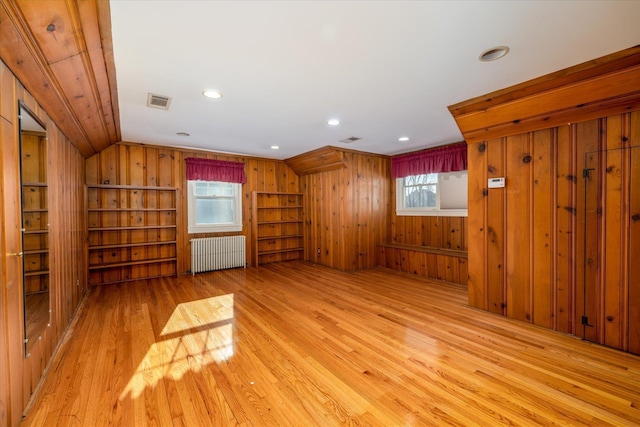 unfurnished living room featuring radiator heating unit, a healthy amount of sunlight, wooden walls, and vaulted ceiling