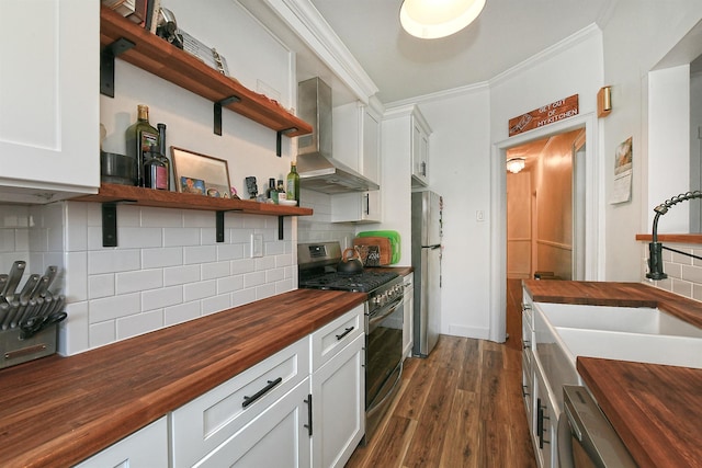 kitchen with appliances with stainless steel finishes, tasteful backsplash, wall chimney range hood, white cabinets, and wood counters