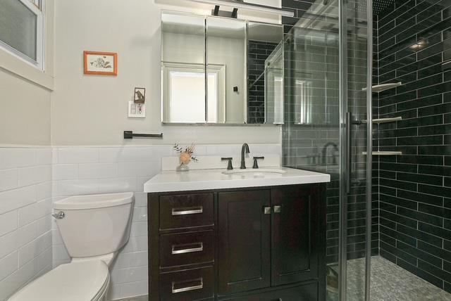 bathroom featuring a shower with door, tile walls, toilet, and vanity