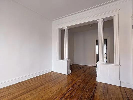 empty room featuring decorative columns, crown molding, and dark hardwood / wood-style floors