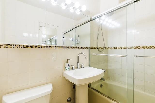 bathroom with toilet, enclosed tub / shower combo, tile walls, and decorative backsplash