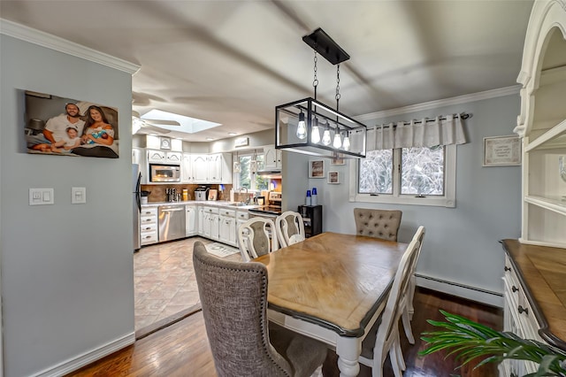 dining space with a skylight, a baseboard heating unit, ceiling fan, crown molding, and sink