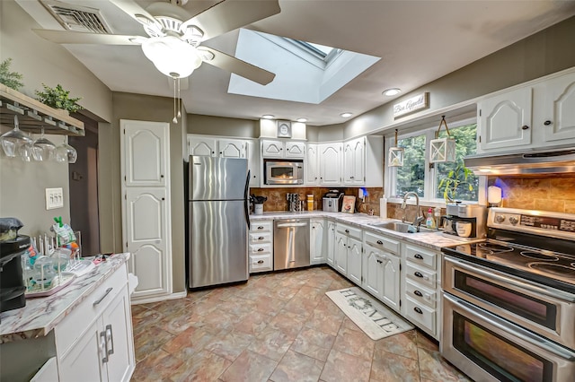 kitchen with white cabinets, a skylight, stainless steel appliances, tasteful backsplash, and sink