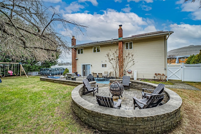 back of property featuring a patio area, a playground, a lawn, an outdoor fire pit, and a swimming pool