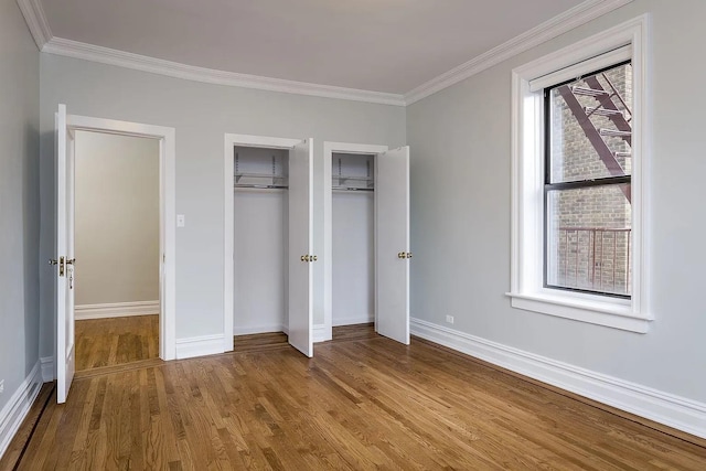 unfurnished bedroom featuring hardwood / wood-style flooring, ornamental molding, and multiple closets