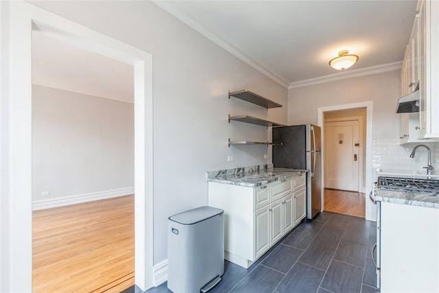 kitchen featuring appliances with stainless steel finishes, tasteful backsplash, white cabinetry, light stone counters, and crown molding