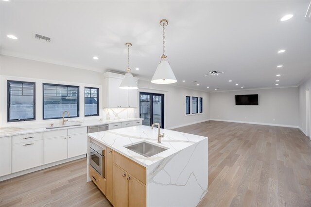 kitchen with sink, an island with sink, white cabinetry, and light stone counters