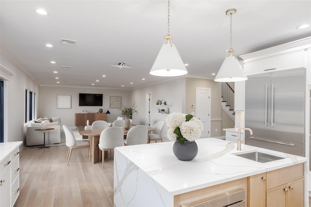 kitchen with built in fridge, pendant lighting, sink, a kitchen island with sink, and light stone counters