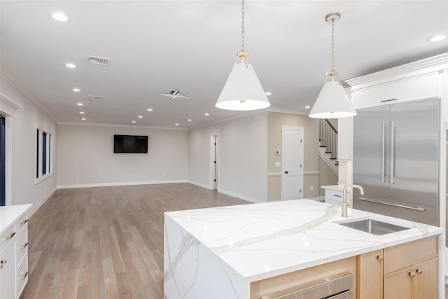 kitchen featuring built in refrigerator, light stone countertops, decorative light fixtures, an island with sink, and sink