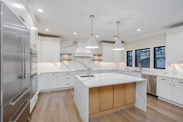 kitchen with pendant lighting, appliances with stainless steel finishes, custom exhaust hood, white cabinets, and a center island with sink