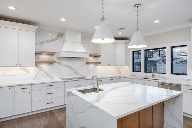 kitchen with custom exhaust hood, a kitchen island with sink, and white cabinetry