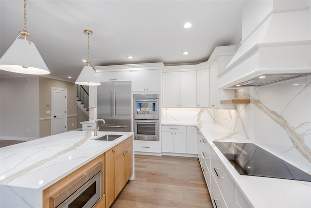 kitchen featuring white cabinetry, built in appliances, an island with sink, premium range hood, and sink