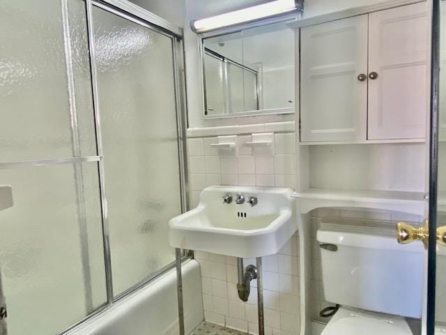 full bathroom with bath / shower combo with glass door, sink, tile walls, and toilet