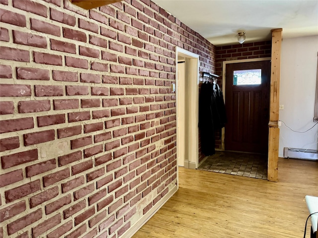 foyer entrance featuring a baseboard heating unit, light hardwood / wood-style flooring, and brick wall